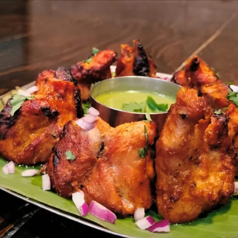 Kumar's Express Indian chicken tikka with green chutney, red onions, and cilantro on a banana leaf.