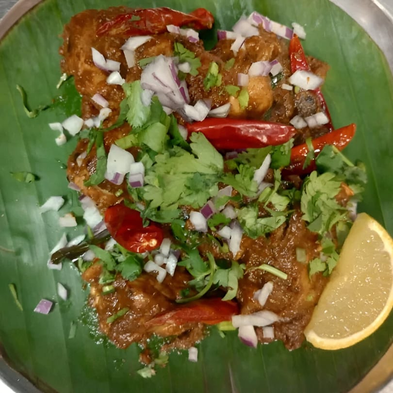 Kumar's Express Indian dish with chicken, red chilies, onions, cilantro, and a lemon wedge on a banana leaf.