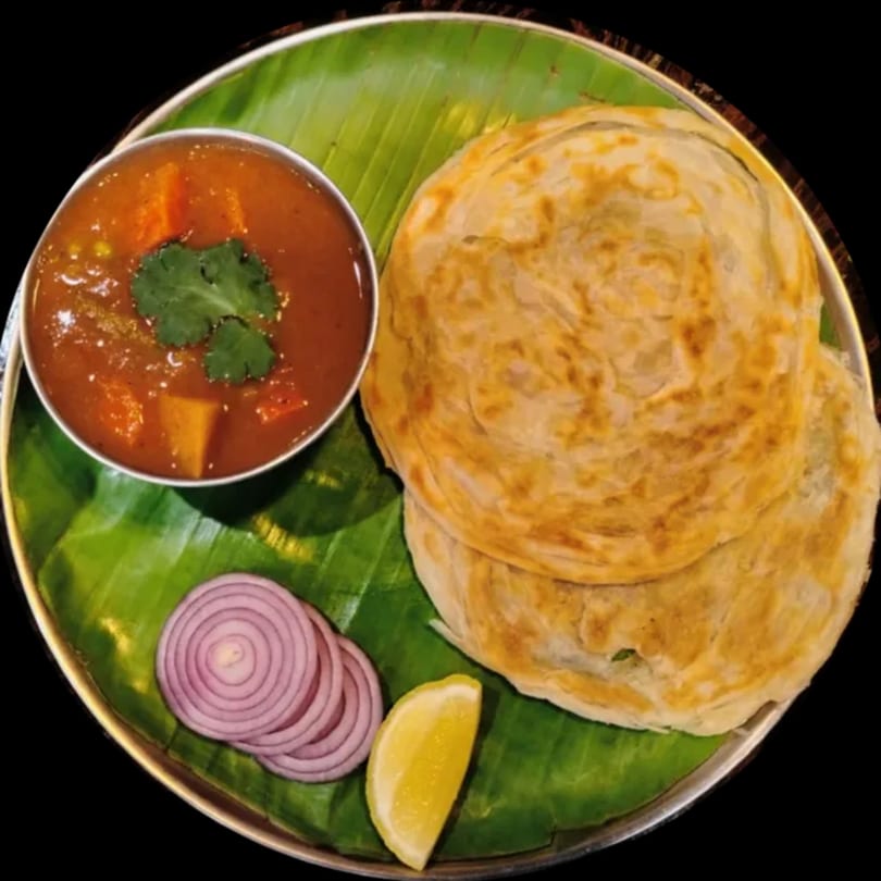 Indian paratha with curry, sliced red onions, and a lemon wedge on a banana leaf.