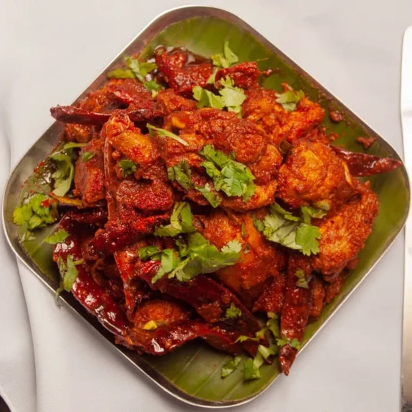 Kumar's Express Chicken 65, a spicy red Indian chicken dish with green cilantro on a banana leaf.