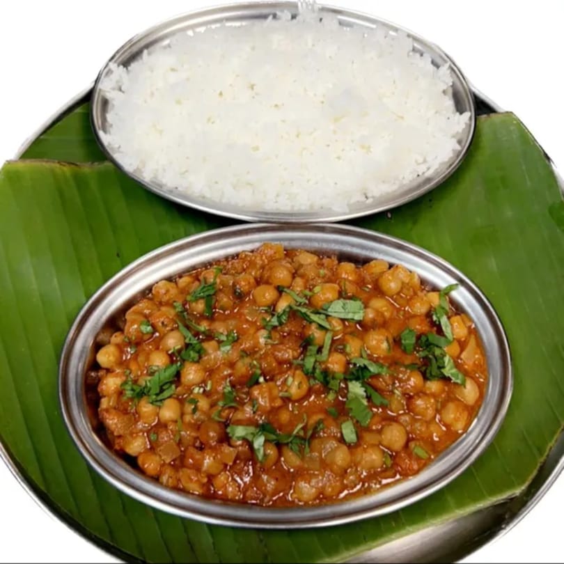 Kumar's Express chana masala and white rice served in metal bowls on a banana leaf.
