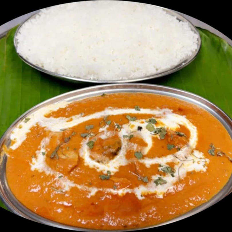 Indian butter chicken with cream and herbs, served with white rice on a banana leaf.