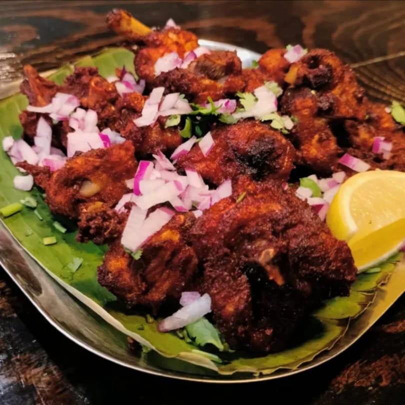 Kumar's Express Indian chicken 65, garnished with red onions, cilantro, and a lemon wedge.